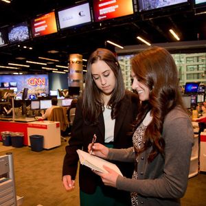 Two students write in a notebook in a newsroom.